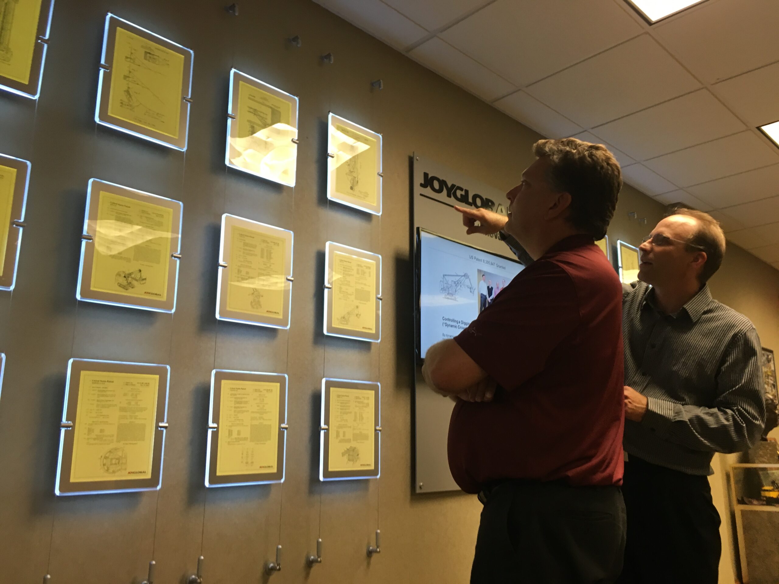 Man observing framed awards on a wall in a museum or gallery.