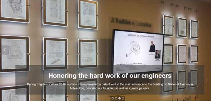 A worker paints a wall mural honoring engineers at a company entrance.